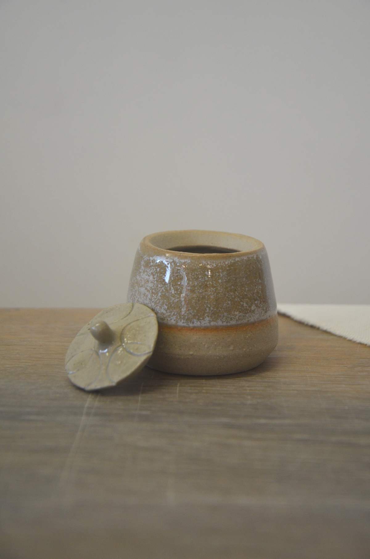 Pot beige moucheté, son couvercle posé à côté.