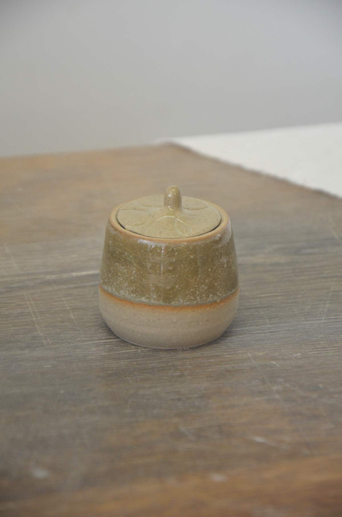 Petit pot à couvercle vert-brun sur une table en bois.
