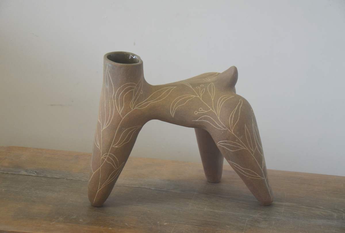 Pièce brune à quatre pieds ornée de feuillages blancs, posée sur une table en bois.