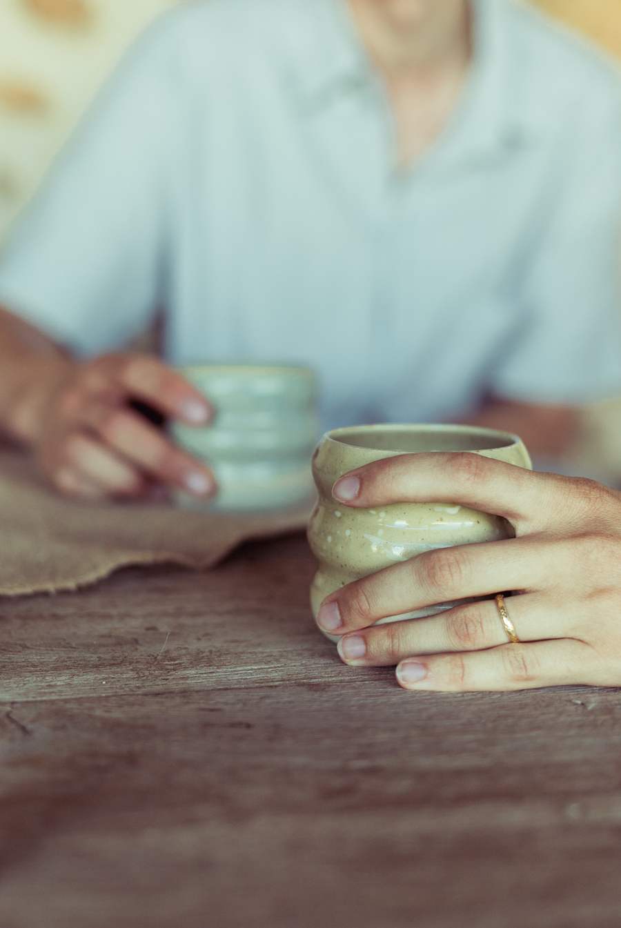 Deux mains tiennent deux tasses aux émaux vert clair.